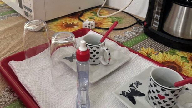 A tray with a mug, a glass, a water bottle, and a fork on a table with a floral tablecloth. - Pousada simples  (Pinhais)