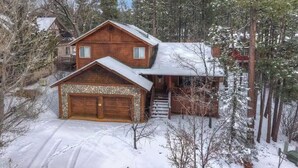 Une cabane en bois à deux étages, avec des fondations en pierre, un garage et un escalier menant à un porche.