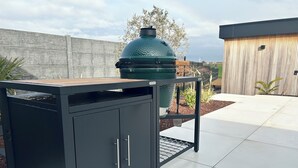 A black outdoor kitchen with a grill, a metal rack, and a cabinet with drawers. - Inspire Residence and Wellness (Tongeren-Borgloon)