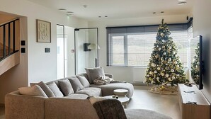 A modern living room with a sectional sofa, a Christmas tree, and a flat-screen TV. - Inspire Residence and Wellness (Tongeren-Borgloon)