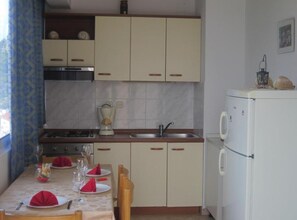 A compact kitchen with a dining area set for four, including a stove, sink, and refrigerator. - One-Bedroom Apartment with Terace with Sea View (Hvar)