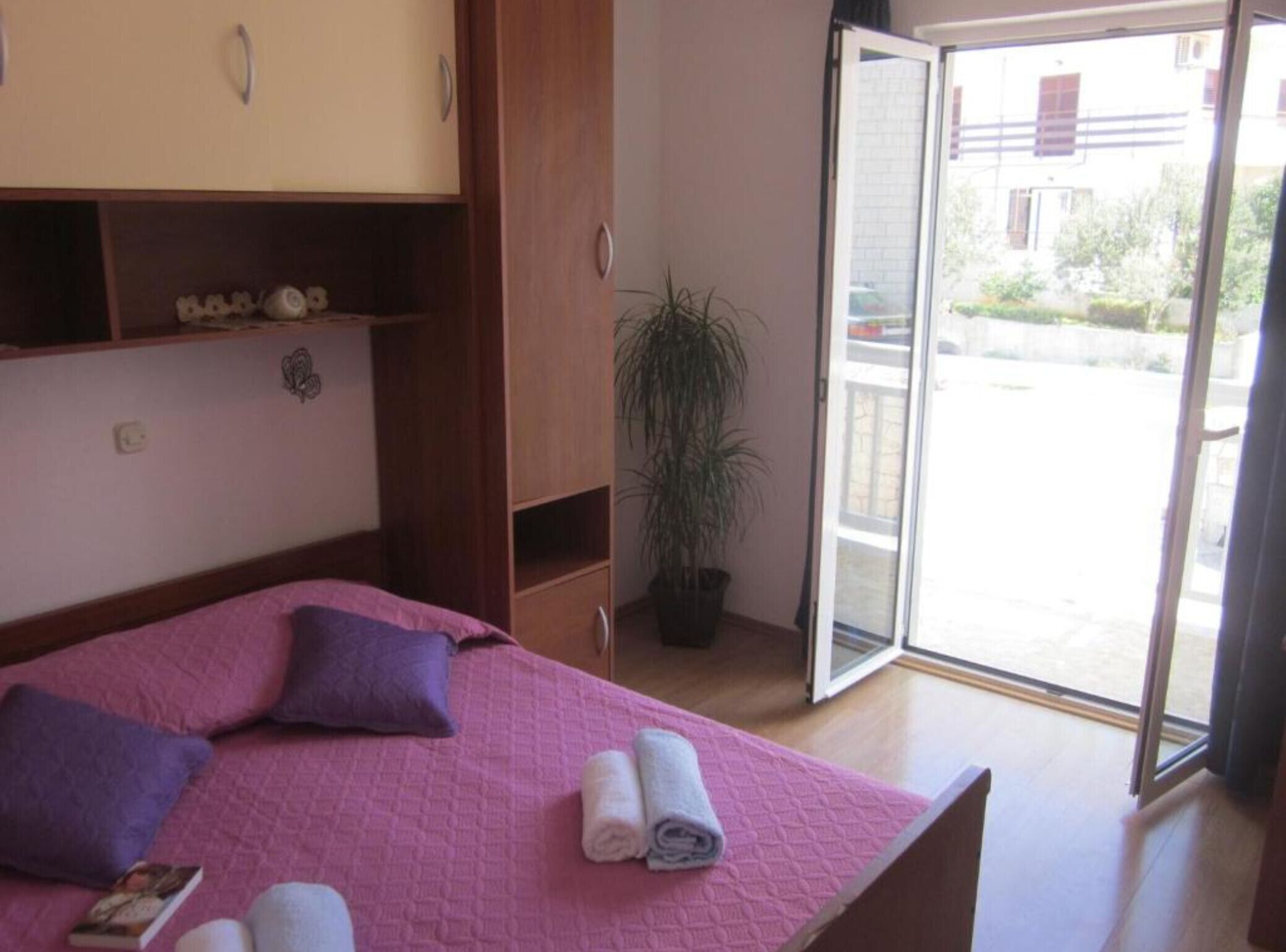 A bedroom with a bed, a potted plant, and a sliding glass door to the outside.