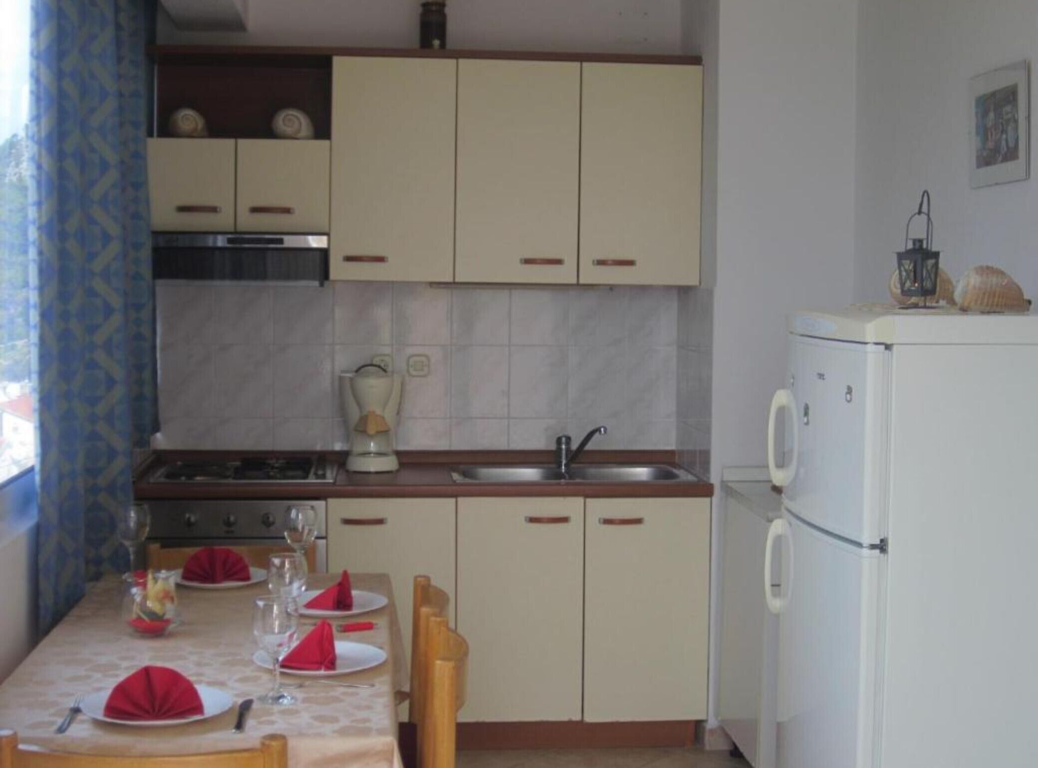 Una cuina compacta amb zona de menjador preparada per a quatre, inclosa una placa de cocció, un rentaplat i un frigorífic.