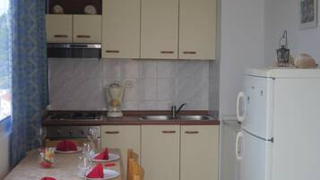 Una cuina compacta amb zona de menjador preparada per a quatre, inclosa una placa de cocció, un rentaplat i un frigorífic.