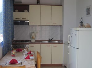 A compact kitchen with a dining area set for four, including a stove, sink, and refrigerator. - Azure Hvar Residence - Studio with sea view (Hvar)
