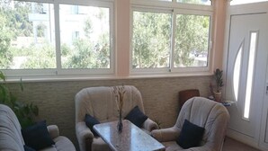 Ein Zimmer mit zwei beigefarbenen Sessel, einem kleinen Tisch mit einer Vase und Blick ins Grüne durch große Fenster.