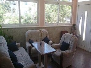 Ein Zimmer mit zwei beigefarbenen Sessel, einem kleinen Tisch mit einer Vase und Blick ins Grüne durch große Fenster.