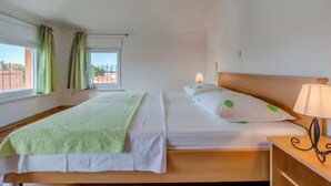 Quarto de hotel com duas camas, uma janela com cortinas, mesa de cabeceira com abajur e vista para edifícios.
