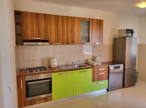 Une cuisine moderne avec des meubles en bois, un plan de travail vert, un réfrigérateur en acier inoxydable et un four encastré.