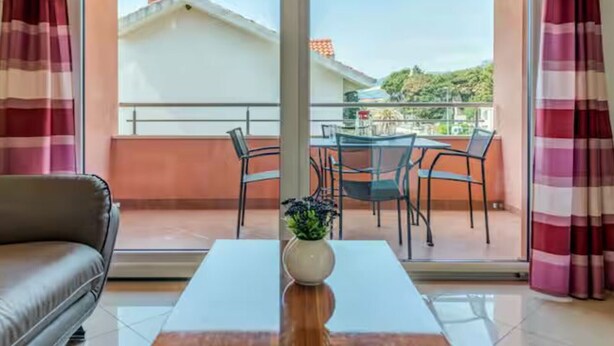 A room with a sofa, a table, and a balcony with a view of buildings and greenery. - Mise Holiday Apartments - Two bedroom apartment II (Kastel Gomilica)