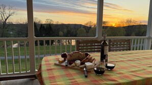 A table set with food and drink on a porch with a scenic view. - Hudson Valley Modern 5 BR Farmhouse with Pond and Stunning Sunsets (Pine Plains)