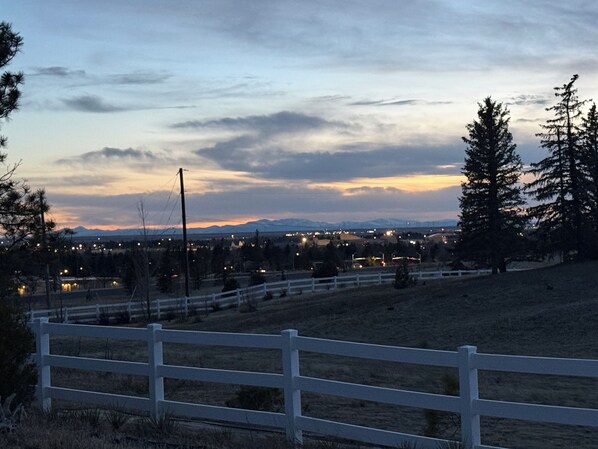 A rural landscape with a white fence, trees, and distant mountains.