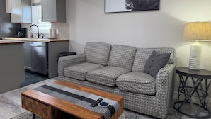 Ein modernes Wohnzimmer mit Sofa, Couchtisch, Küchenzeile und einem gerahmten Bild an der Wand.
