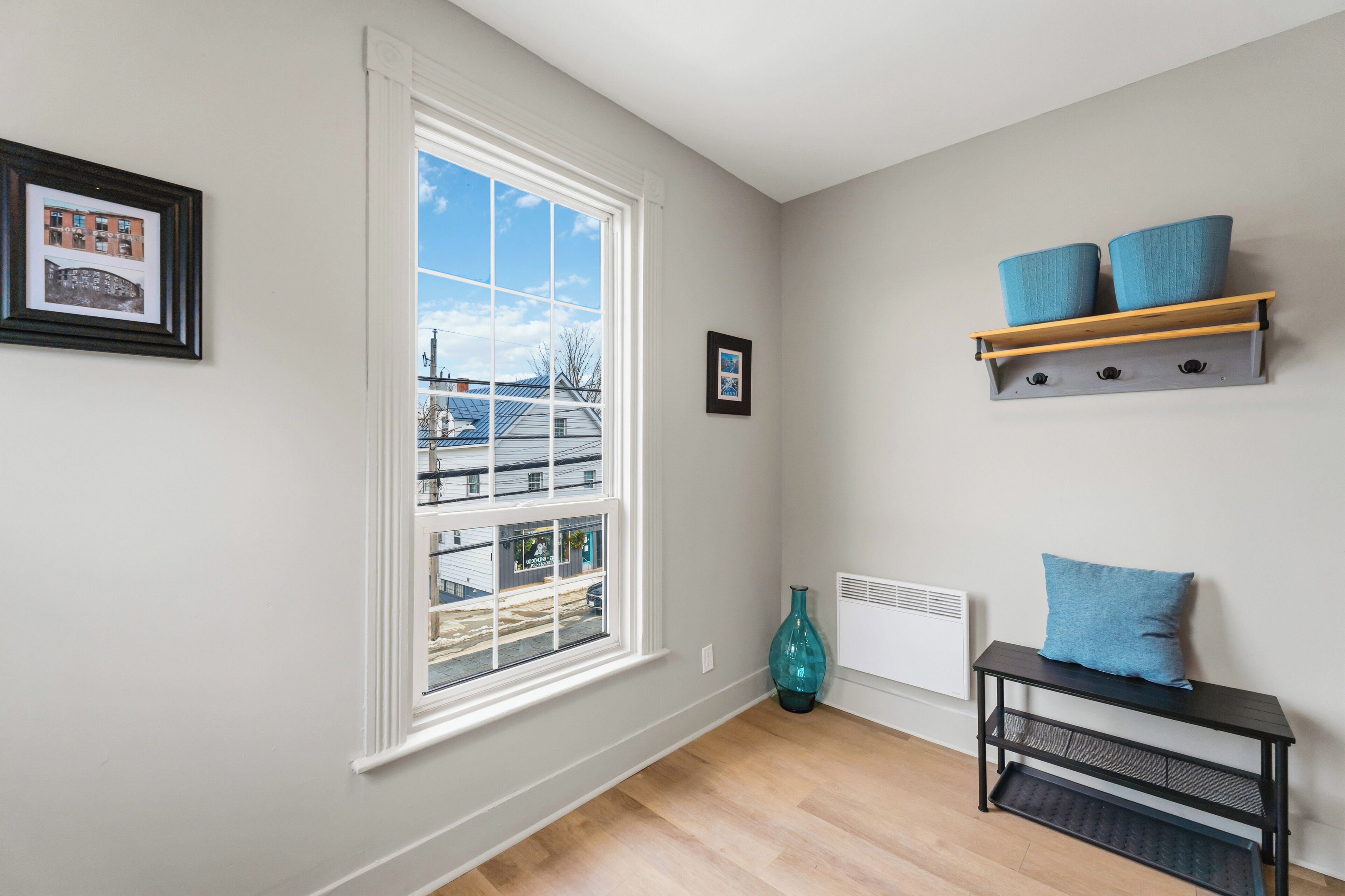 A room with a large window, a radiator, a blue vase, and a black console table with blue cushions.