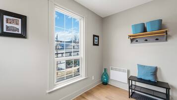 Ein Zimmer mit einem großen Fenster, einem Heizkörper, einer blauen Vase und einem schwarzen Konsolentisch mit blauen Kissen.