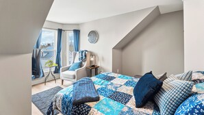 Een slaapkamer met een bed, een stoel, een klein tafeltje, een klok en een raam met gordijnen.