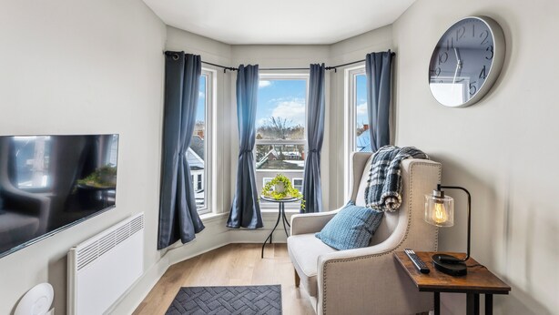 Een hoekappartement met een televisie, een klok, een bank, een lamp en uitzicht op gebouwen.