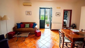 Een woonkamer met een bank, salontafel en eettafel. Er is een deur naar een balkon met uitzicht op groen.