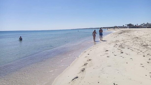 A beach with clear water, a sandy shore, and a few people walking. - Cozy Apartment Very Close to the Beach (Hammamet)