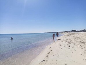 A beach with clear water, a sandy shore, and a few people walking. - Cozy Apartment Very Close to the Beach (Hammamet)