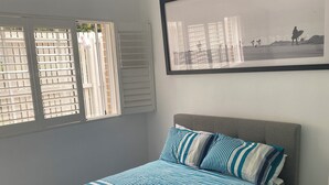 Una camera da letto con un letto, una ventola a soffitto, una finestra con persiane e un quadro appeso al muro.