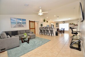 A living room with a sofa, coffee table, and chairs, a dining area with a table and chairs, a kitchen with appliances, and a ceiling fan.