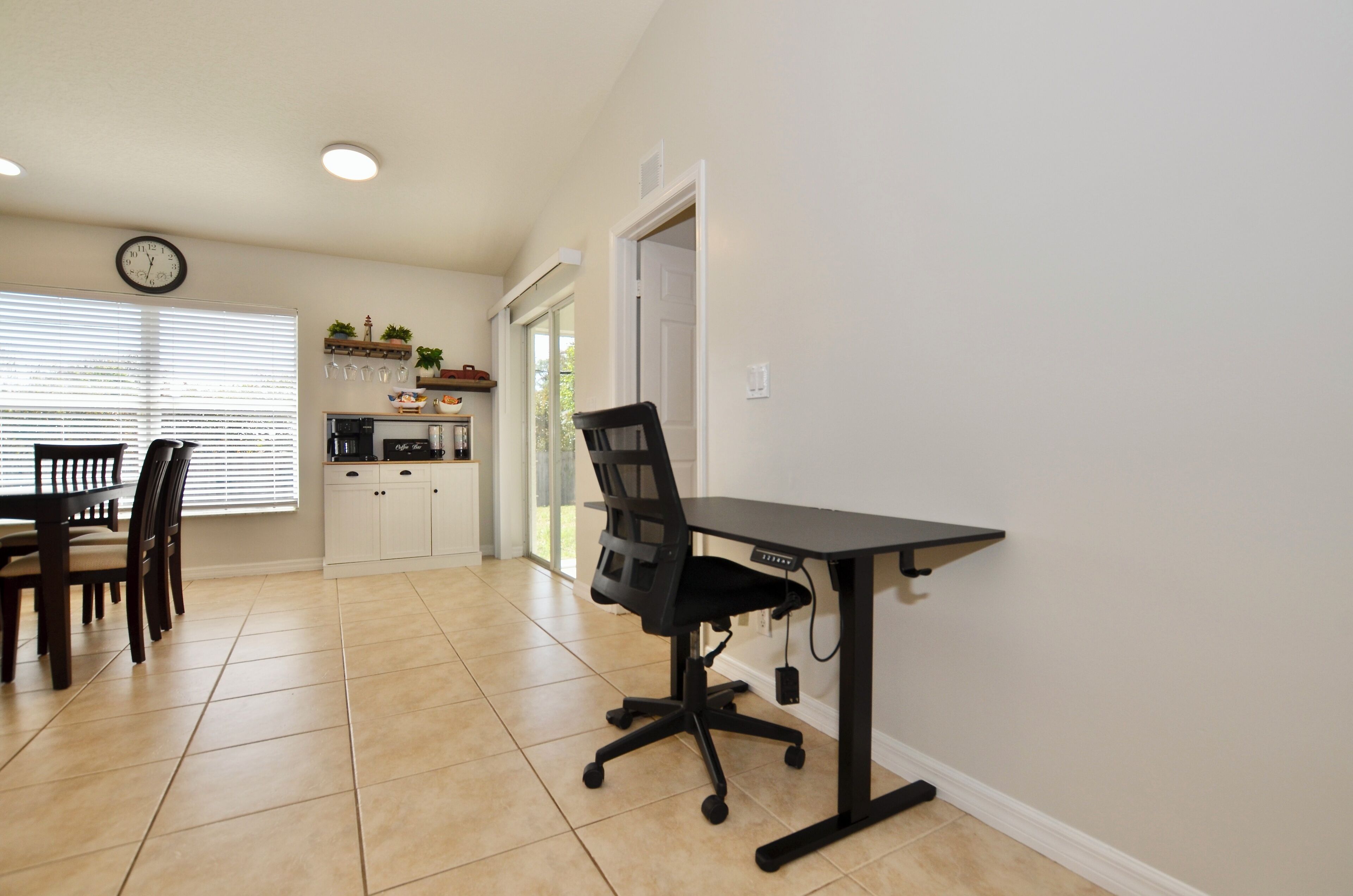 A dining area with a table and chairs, a kitchen with appliances, and a clock on the wall.