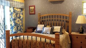 Une chambre à coucher avec un lit en bois, des rideaux à motifs floraux, une table de chevet avec une lampe et un climatiseur fixé au mur.