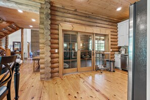A log cabin interior with a wooden floor, a dining area with a table and chairs, a kitchen with cabinets and a refrigerator, and a sliding glass door leading to an outdoor area. - Gorgeous 4-bedroom cabin on the lake  in fabulous Fall Creek Falls! (Fall creek Falls)