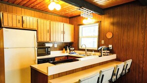 Une cuisine dotée de meubles en bois, d’un réfrigérateur, d’un four à micro-ondes, d’un évier et d’un coin bar avec des chaises.