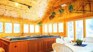 Une cabane en bois avec une grande baignoire en bois, des chaises blanches et des plantes en pot.