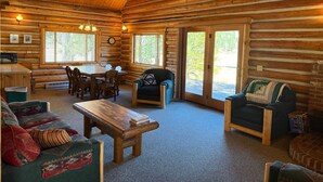 A log cabin interior with a dining area, two sofas, a coffee table, and a fireplace.