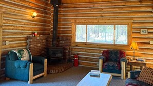 A log cabin interior with a fireplace, two sofas, a coffee table, and a window with a view.