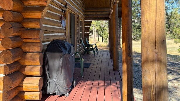 A wooden log cabin with a covered porch, outdoor seating, and a grill.