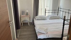 A bedroom with a bed, a desk, a chair, a lamp, and a door. - Noonbir Alaçatı (Cesme)