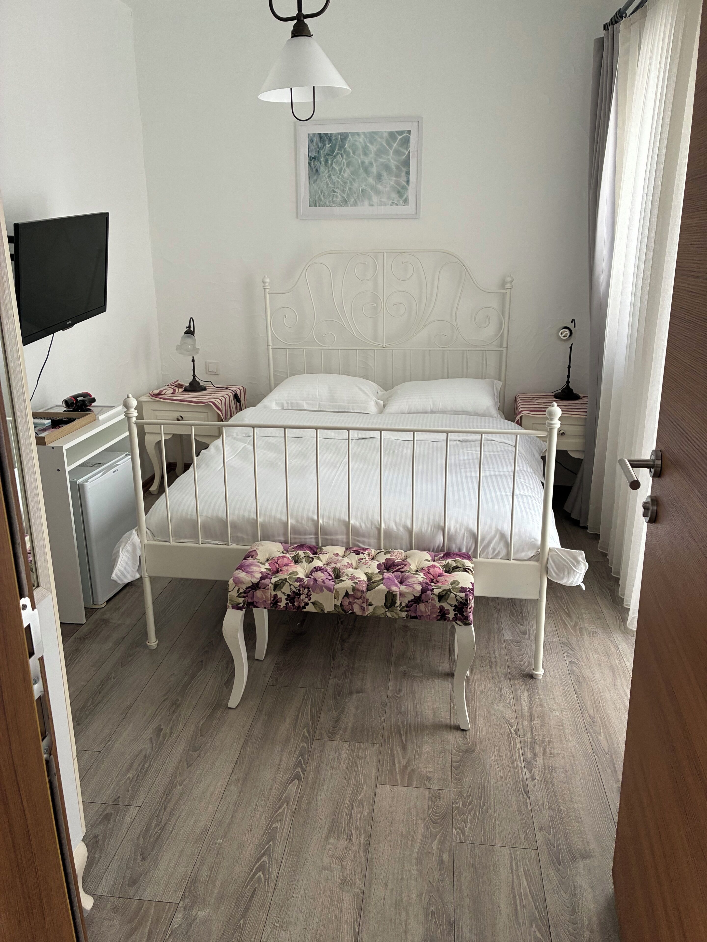 Un dormitorio con una cama, mesitas de noche, un banco, un televisor y una lámpara en el techo.