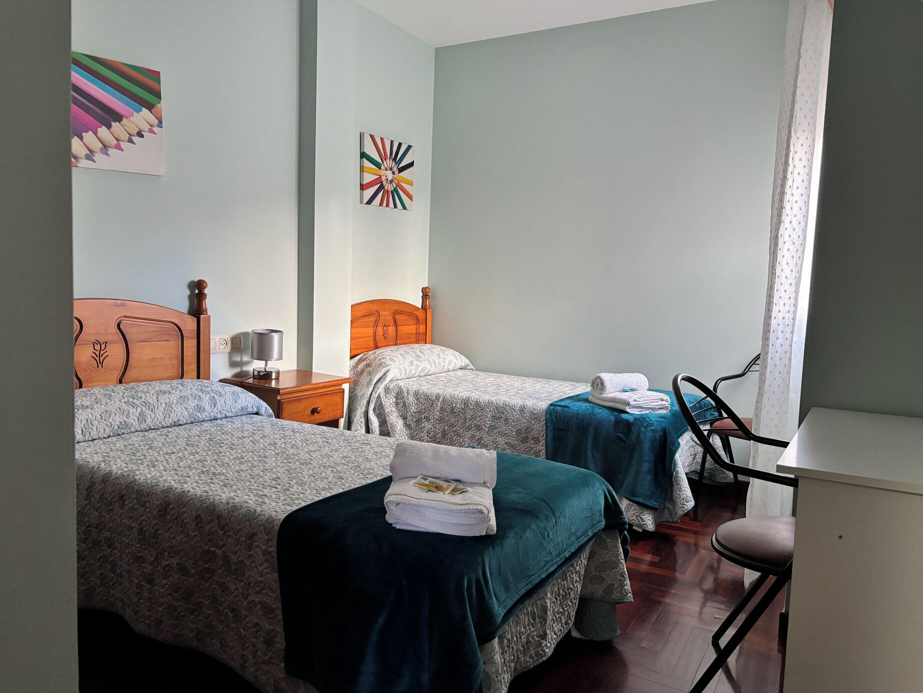 Habitación de hotel con dos camas, un escritorio, una silla y obras de arte en las paredes.