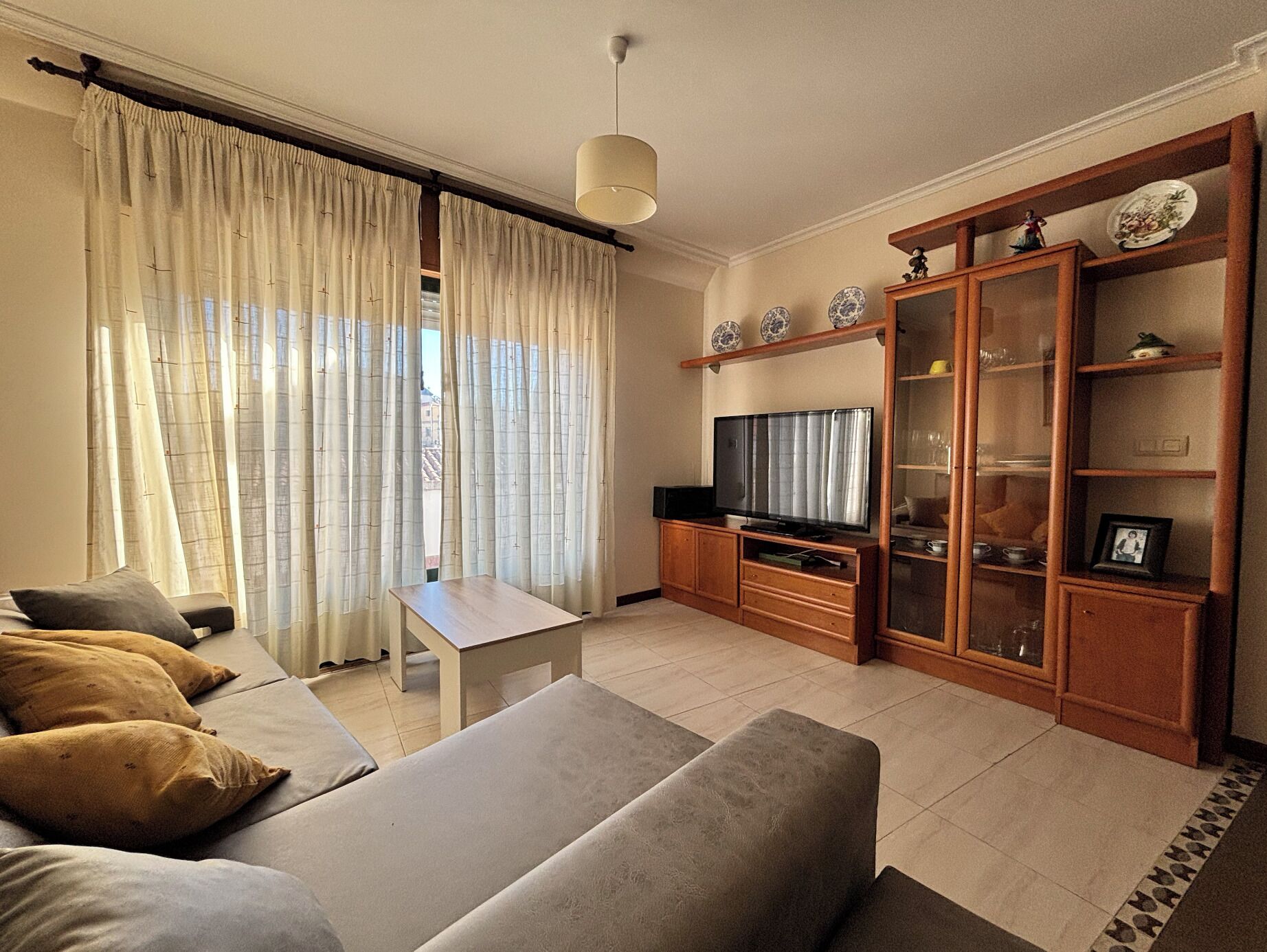 A living room with a sofa, a table, a TV, and a cabinet with decorative items.