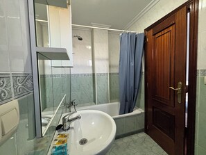 A bathroom with a bathtub, a sink, a mirror, and a door. - Golfiño Apartment (O Grove)