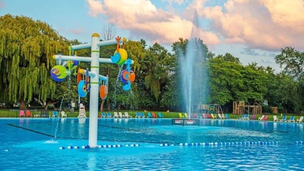 Una piscina con zona de juegos acuáticos, que incluye una fuente y coloridos elementos.