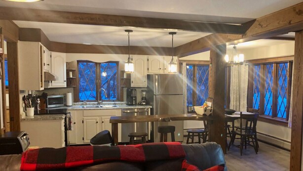 Une cuisine moderne équipée d’appareils électroménagers en acier inoxydable, un coin repas avec une table et des chaises, et un salon confortable avec un canapé en cuir et des coussins décoratifs.