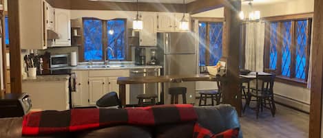 A modern kitchen with stainless steel appliances, a dining area with a table and chairs, and a cozy living room with a leather sofa and decorative pillows.