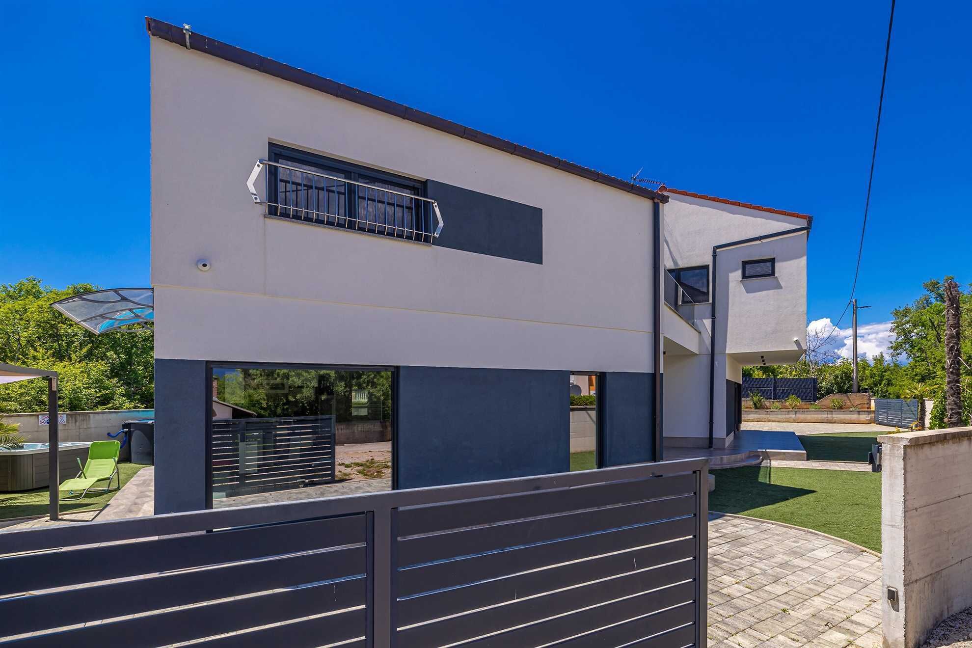 Une maison moderne à deux étages, dotée d’un balcon, d’un garage et d’un espace extérieur clôturé.