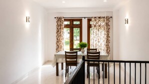 Un comedor con una mesa dispuesta para cuatro personas, una planta en maceta y cortinas con estampado floral.