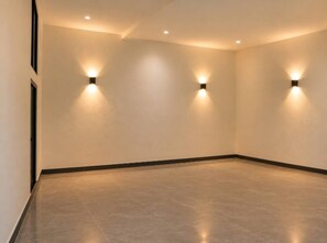 A room with a polished floor, recessed ceiling lights, and wall-mounted sconces.