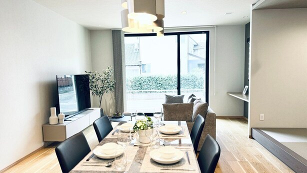 A modern dining area with a long table, chairs, and a television on a stand.