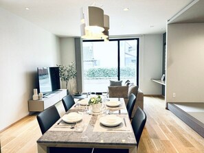 Uma sala de jantar moderna com uma mesa comprida, cadeiras e uma televisão sobre um suporte.