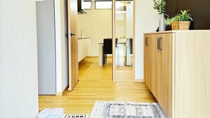 A hotel corridor with wooden flooring, a tiled entrance, a sliding door, and a reception area with a plant.