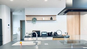A modern kitchen with a central island, built-in appliances, and a wooden shelf above.