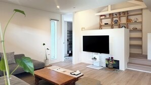 A modern living room with a flat-screen TV, a sofa, a coffee table, and a bookshelf. - Akikawa Miyoshi 1 | 20 min to TSMC | Entire 3LDK House | Up to 6 Guests (Koshi)